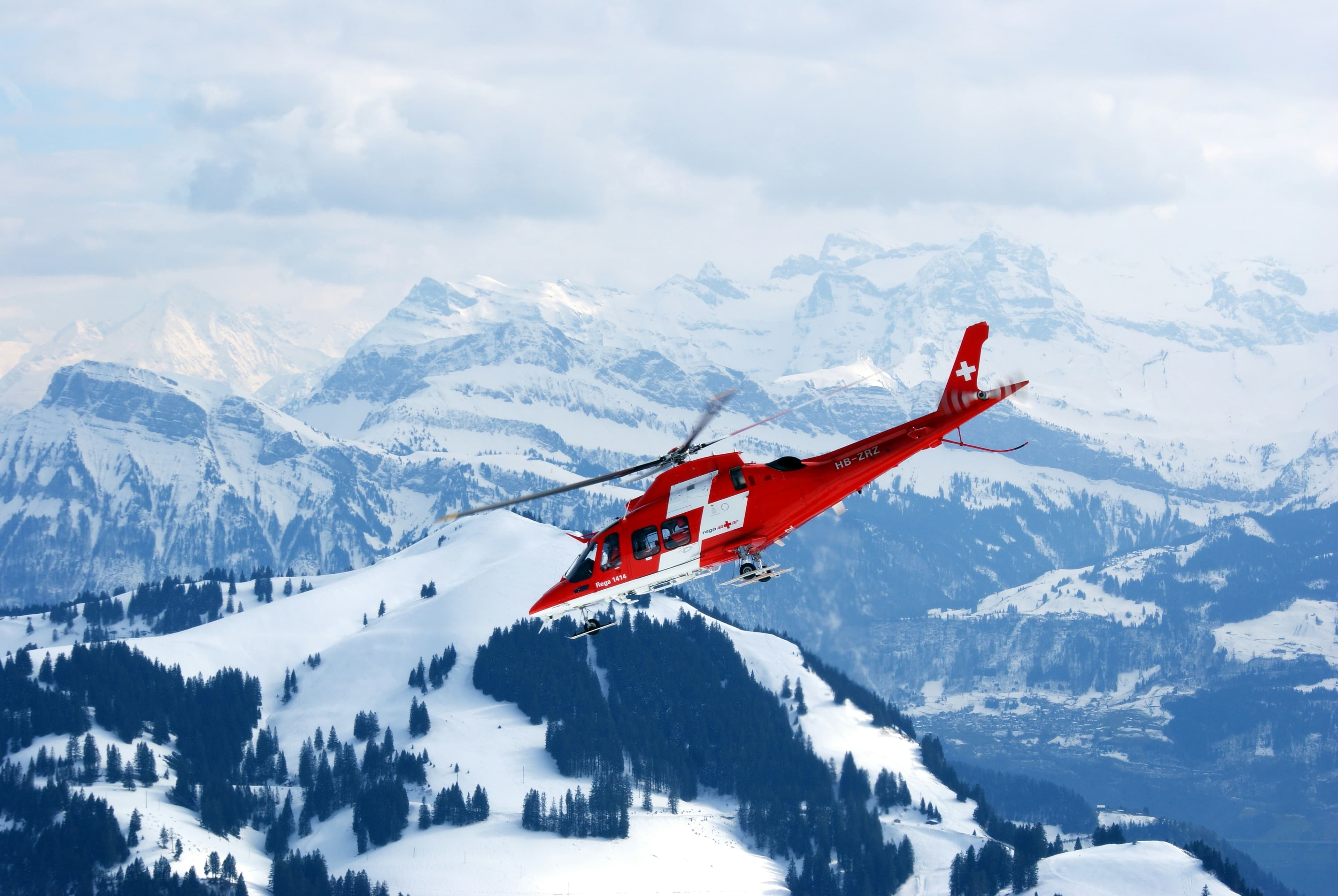 Un elicottero rosso in volo davanti a montagne e boschi innevati