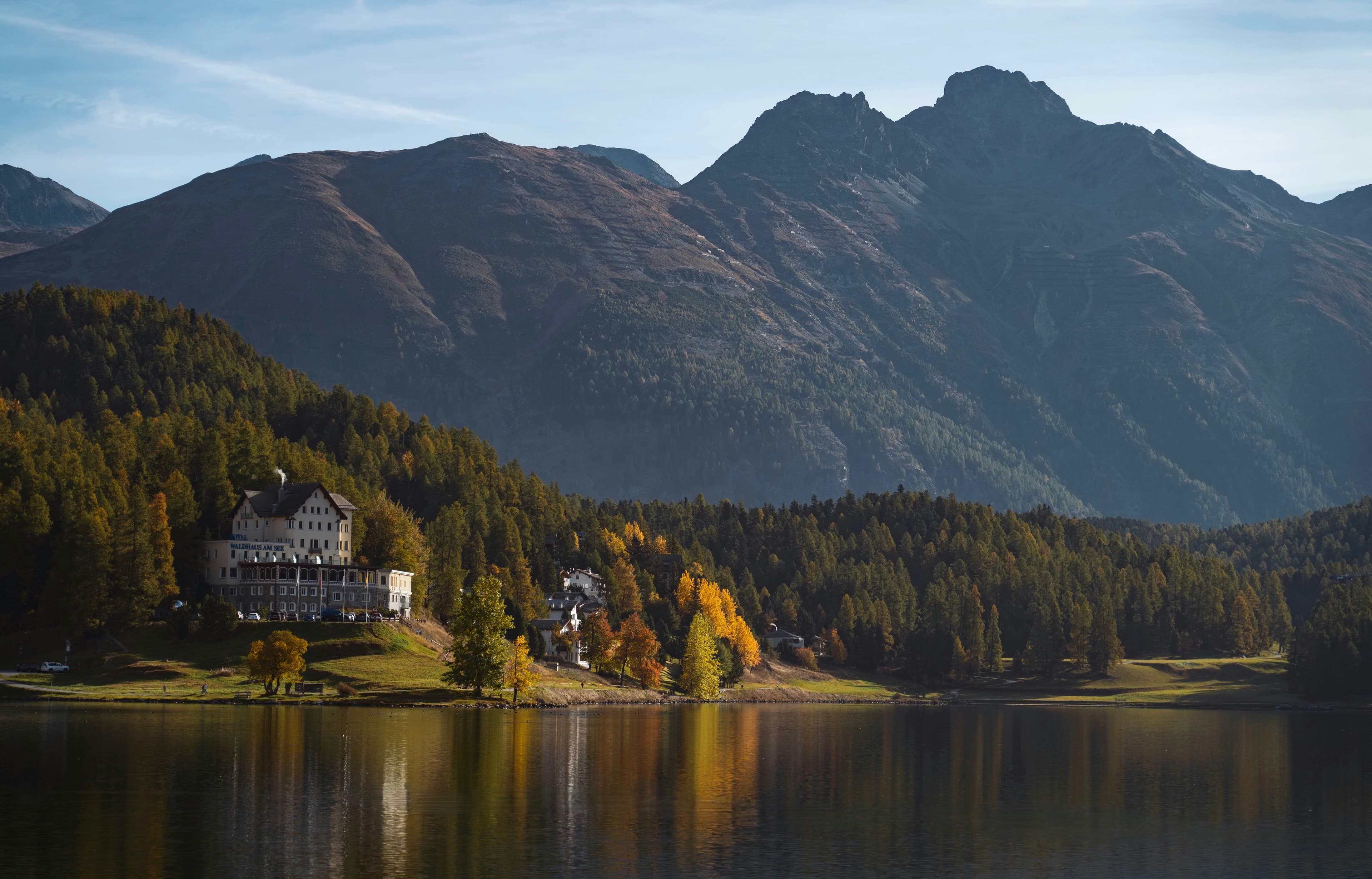Un lago alpino ai piedi delle montagne, con alberi dorati e riflessi sull’acqua