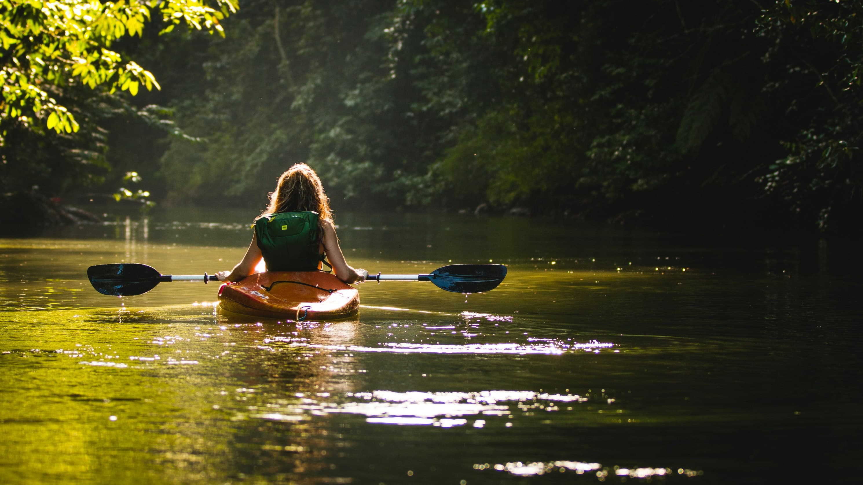 Una persona in kayak sulle acque calme, tra alberi e riflessi di sole.