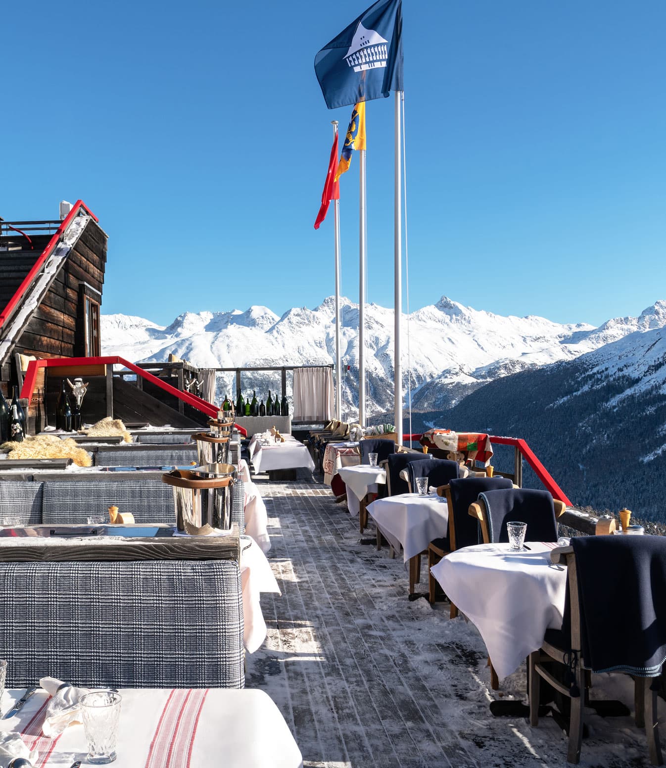 Una terrazza con tavoli apparecchiati e sedute all’aperto, affacciata sulle montagne innevate