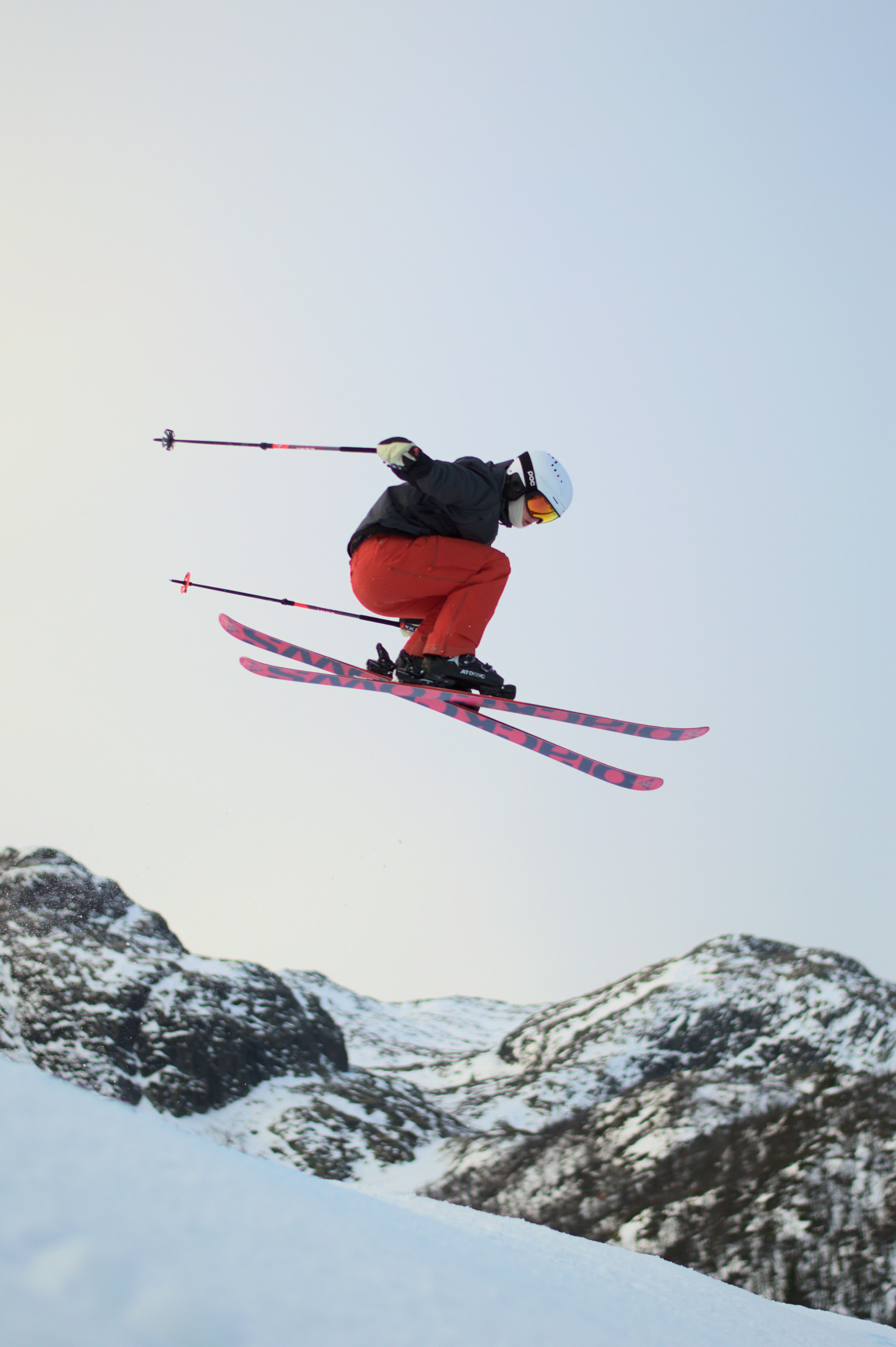 Uno sciatore con pantaloni rossi in salto sopra le rocce innevate