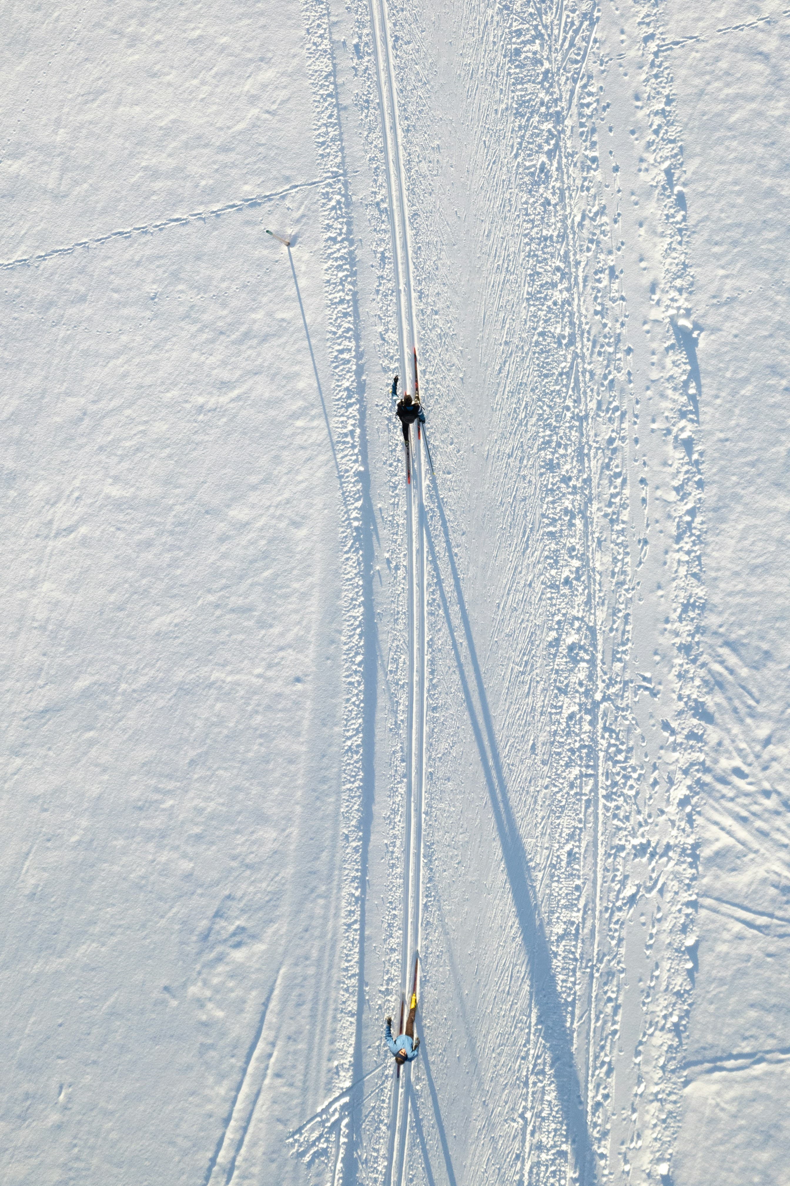 Due sciatori di fondo ripresi dall’alto lungo i binari nella neve, con ombre allungate
