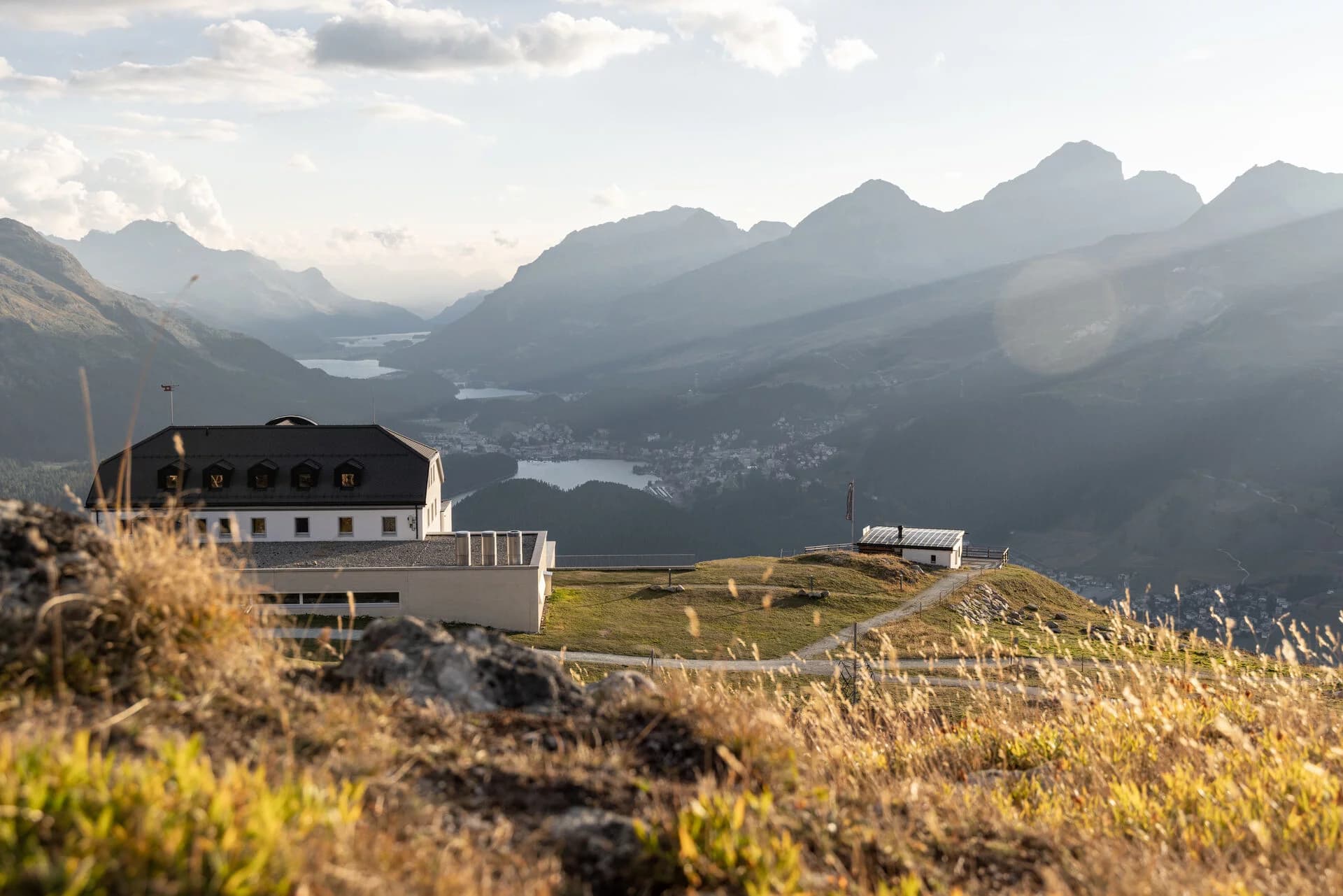 L’edificio di Muottas Muragl tra prati e sentieri, con i laghi e le montagne dell’Engadina sullo sfondo.